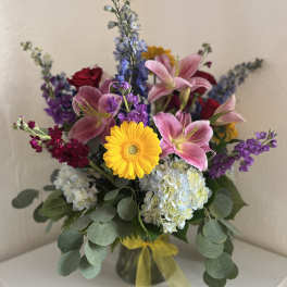 Mixed bouquet with pink lilies, yellow gerbera daisy, hydrangeas, and purple flowers in a vase