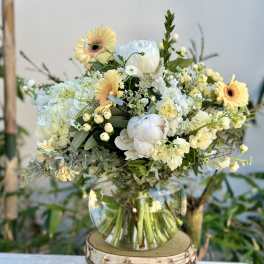 Mixed bouquet of pale yellow and white flowers in a clear glass vase