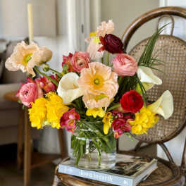 Colorful bouquet in a clear glass vase with poppies, ranunculus, calla lilies, and yellow blooms