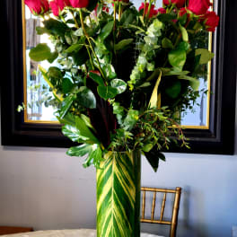 Tall vase arrangement of red roses with mixed greenery