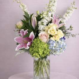 Mixed bouquet of lilies, roses, hydrangea, and white spikes in a glass vase
