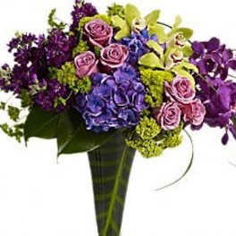 Bouquet of purple roses, blue hydrangeas, and green orchids in a tall vase