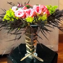 Pink roses in a tall glass vase with dark spiky foliage