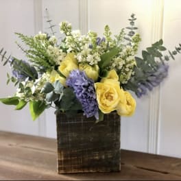 Yellow and lavender flowers arranged in a square wooden vase