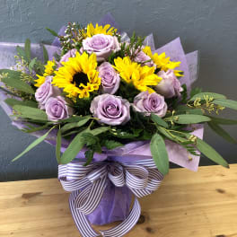 Lavender roses and yellow sunflowers in a wrapped bouquet with a striped ribbon