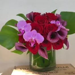 Red roses and purple orchids arranged in a glass vase