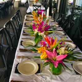 Tropical floral centerpieces on a long banquet table with plates and candles