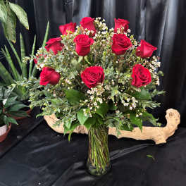 Red roses arranged in a clear glass vase with small white filler flowers