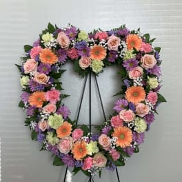 Heart-shaped floral wreath with pink, purple, and orange blooms on a stand