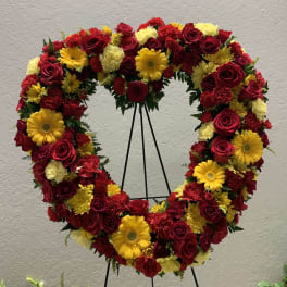 Heart-shaped floral wreath with red roses and yellow daisies on a stand
