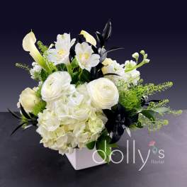 White floral arrangement in a square vase with calla lilies and hydrangeas