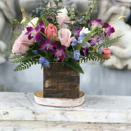 Rustic wood box arrangement with pink roses, tulips, purple orchids, and blue blooms