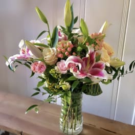 Mixed bouquet of pink lilies, roses, and spray roses in a clear glass vase