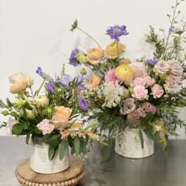 Two pastel floral arrangements in white containers on a table