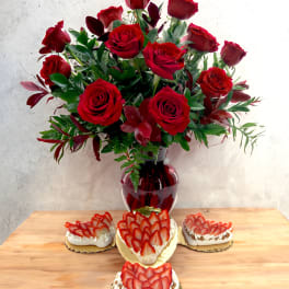 Red rose bouquet in a red vase with strawberry-topped desserts on a table