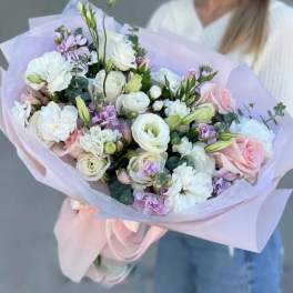 Handheld bouquet of white and blush flowers wrapped in pale lavender paper