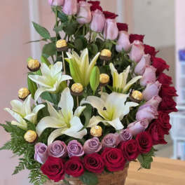 Basket arrangement of red and lavender roses with white lilies and gold chocolates