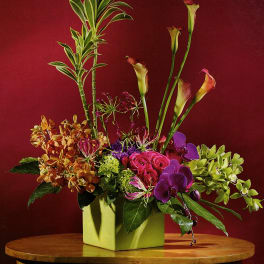 Colorful floral arrangement in a square green vase with tall calla lilies