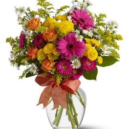 Mixed bouquet of pink, orange, yellow, and white flowers in a glass vase