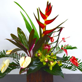 Tropical floral arrangement with red heliconia, anthuriums, and orchids in a wooden vase