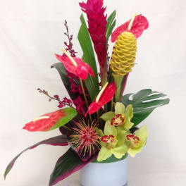 Tropical flower arrangement in a white vase with red anthuriums and yellow orchids