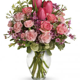 Pink tulips, roses, and carnations arranged in a clear glass vase