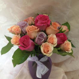 Bouquet of pink, peach, and lavender roses in a purple vase with a ribbon