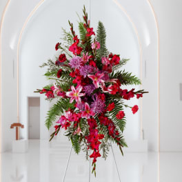 Tall pink and red floral arrangement on a stand in a white interior