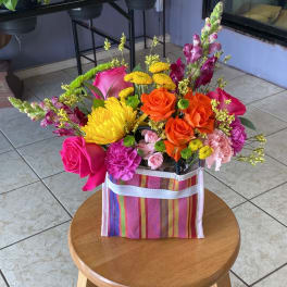 Bright mixed bouquet in a striped gift bag with roses, chrysanthemums, and snapdragons