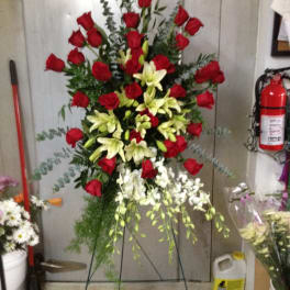 Standing floral spray with red roses and pale lilies on a metal easel