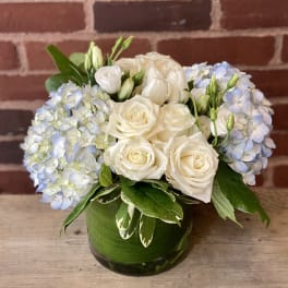 White roses and pale blue hydrangeas in a green glass vase