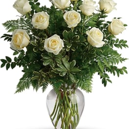 White roses arranged in a clear glass vase with dense greenery