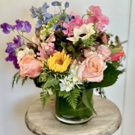 Mixed bouquet in a green glass vase with pink, purple, blue, and yellow flowers