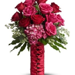 Bouquet of red and pink roses with greenery in a red satin-wrapped vase