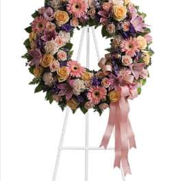Floral wreath on a white stand with pink and yellow blooms and a pink ribbon