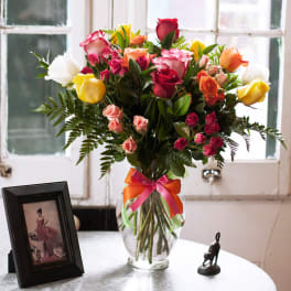 Mixed roses in a clear glass vase with a pink and orange ribbon