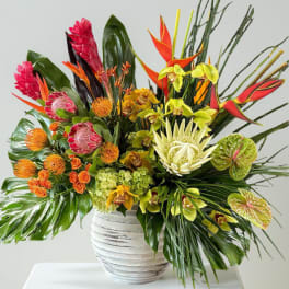 Tropical flower arrangement in a white vase with bright red, orange, yellow, and green blooms