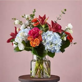 Mixed bouquet of roses, lilies, and hydrangeas in a clear glass vase