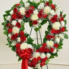 Heart-shaped wreath of red and white flowers on a stand with a red ribbon