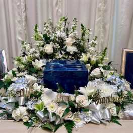 White floral funeral arrangement surrounding a blue urn with memorial name signs