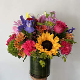 Mixed bouquet with a sunflower, roses, iris, and pink carnations in a glass vase