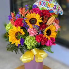Colorful bouquet with sunflowers, roses, carnations, and a birthday balloon in a purple vase