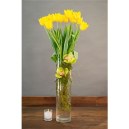 Yellow tulips in a tall glass vase with two green orchids and a small candle