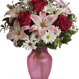 Bouquet of pink lilies, red roses, and white daisies in a pink vase