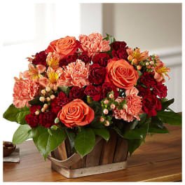 Basket arrangement of orange roses, red carnations, and pink flowers