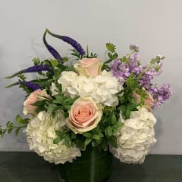 Pink roses with white hydrangeas and purple spikes in a glass vase