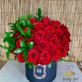 Red roses arranged in a navy hatbox with glossy green leaves