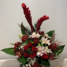 Tropical floral arrangement with red roses and white blooms in a dark vase