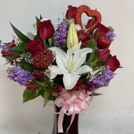 Bouquet of red roses, white lilies, and purple flowers in a vase with pink ribbon