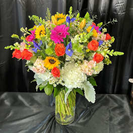 Mixed bouquet of roses, sunflowers, hydrangeas, and irises in a glass vase